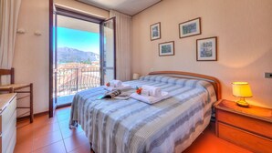 A hotel room with a bed, a nightstand, a chair, a window with a view of mountains, and framed pictures on the wall.