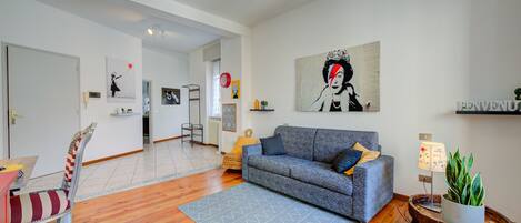 Un salon moderne avec un canapé gris, un parquet en bois et un grand tableau abstrait.