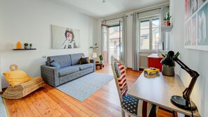 Un salon avec un canapé, une table à manger, une lampe et un petit fauteuil orné d’un drapeau américain.