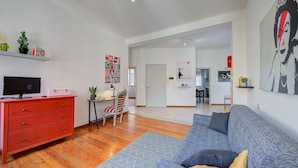 Un salon moderne avec une commode rouge, un canapé gris et un coin repas à l’arrière-plan.