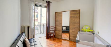 A room with a black leather sofa, a wooden floor, a sliding door, and a small child’s play area with a yellow chair.
