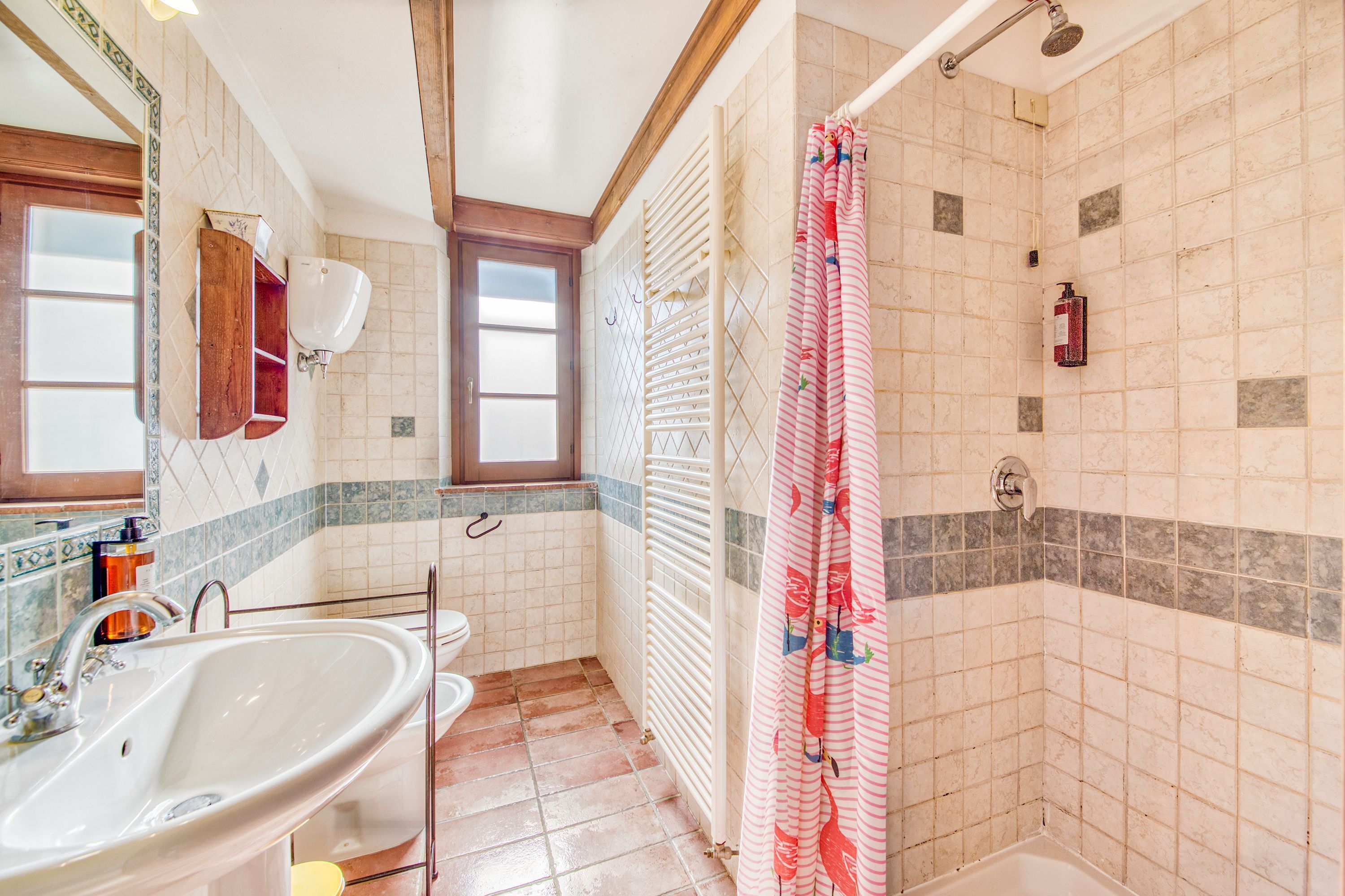 A bathroom with a sink, toilet, shower, and a window.