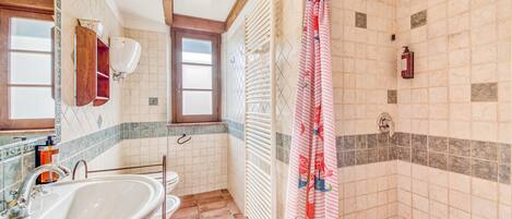 A bathroom with a sink, toilet, shower, and a window.