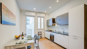Una cocina moderna con armarios blancos, un comedor con una mesa para dos personas y un ventanal que proporciona luz natural.