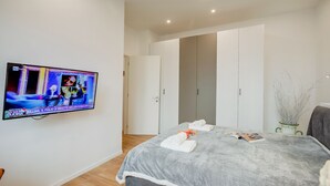 Una habitación de hotel moderna con una cama grande, un televisor de pantalla plana montado en la pared y un armario con puertas correderas.