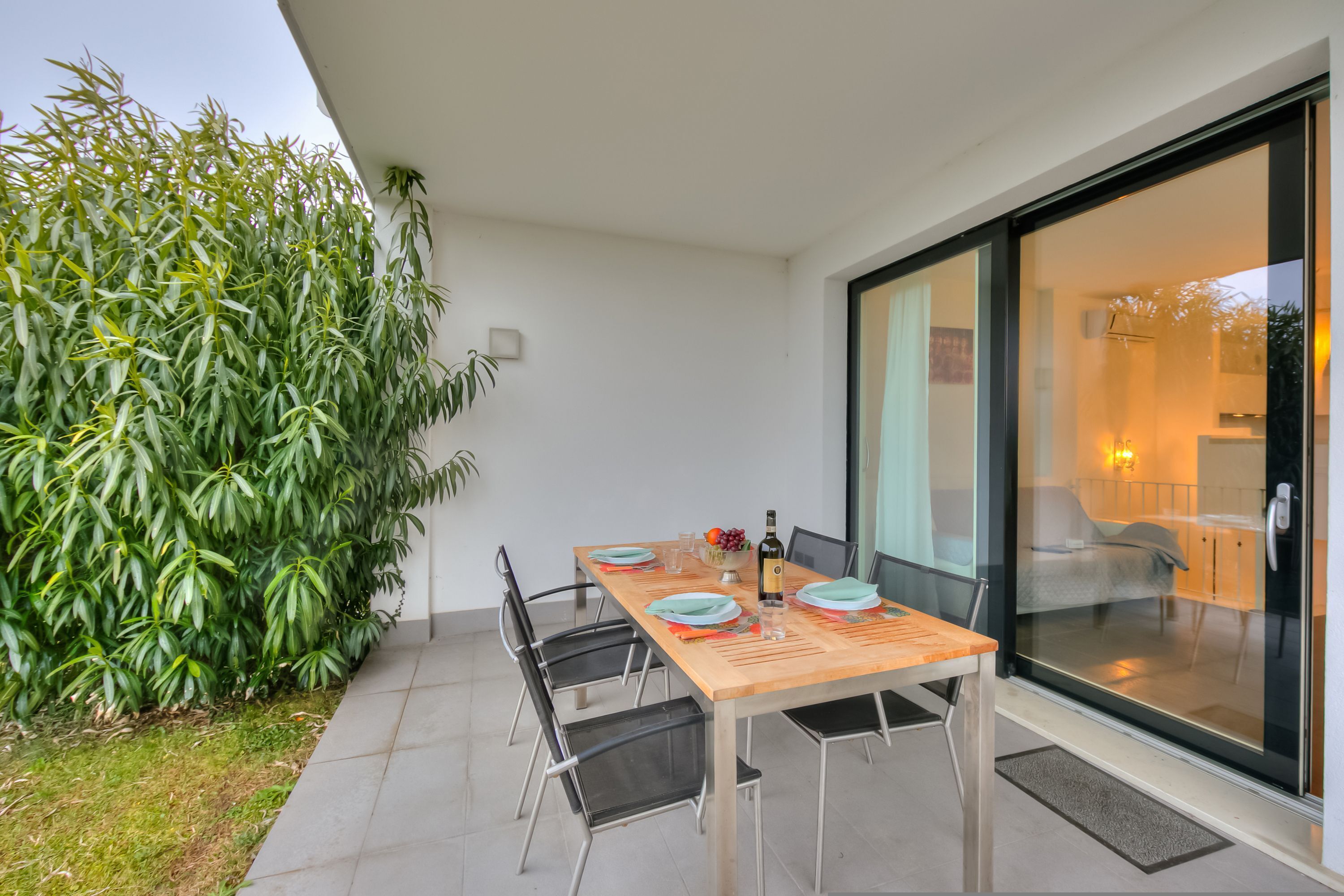 Un coin repas avec une table dressée pour quatre personnes, entourée de chaises, et une grande porte vitrée donnant sur une chambre.