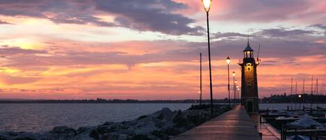 A waterfront promenade with a lighthouse, benches, and a row of street lamps.