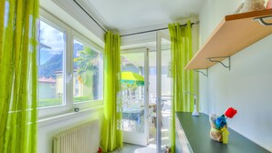 Ein Zimmer mit Blick auf einen Berg, ein Tisch mit Stühlen und ein kleines Regal mit einem Stofftier.