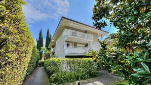 Ein zweistöckiges Wohnhaus mit Balkon, umgeben von gepflegten Hecken und einem gepflasterten Weg.