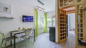 Eine moderne Küche mit Essbereich, einem an der Wand befestigten Fernseher und Blick ins Freie durch große Fenster.