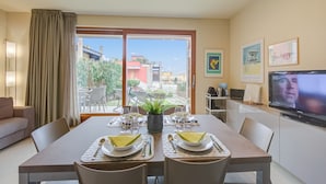 Un coin repas avec une table dressée pour quatre personnes, un téléviseur fixé au mur et une vue sur l’extérieur.