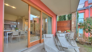 Une maison moderne dotée d’une porte vitrée donnant sur un coin repas et une terrasse avec des fauteuils de jardin.