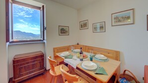 Een eetruimte met een houten tafel gedekt voor vier personen, een raam met uitzicht op bergen en aan de muur hangende foto's.