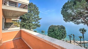 Ein Balkon mit Meerblick, umgeben von Bäumen und einem Gebäude mit einem Balkon.