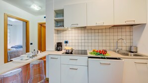 A compact kitchen with white cabinets, a countertop, and a sink. There are two stools and a coffee maker on the counter. - Casa Karin in Riva del Garda (Riva del Garda)