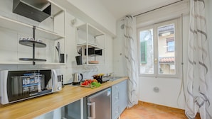 A modern kitchen with a built-in microwave, a coffee machine, and a small refrigerator. There is a window with curtains and a view of the outside. - Riccardo House Stresa (Stresa)