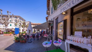 A cobblestone street with outdoor seating, a storefront with a sign reading "PROFUMO DI STRESA," and a variety of bottled products displayed outside. - Riccardo House Stresa (Stresa)