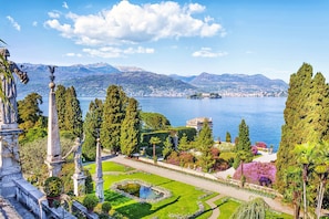 A landscaped garden with statues, a pond, and a view of a lake and mountains. - Riccardo House Stresa (Stresa)