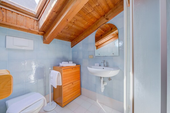 Une salle de bain avec un puits de lumière, un meuble-lavabo en bois, un lavabo blanc et des toilettes.