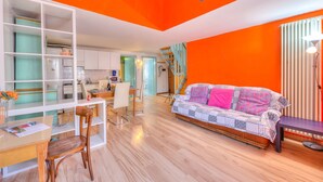 Een lichte oranje kamer met een bank, een eettafel met stoelen en een keukenhoek.