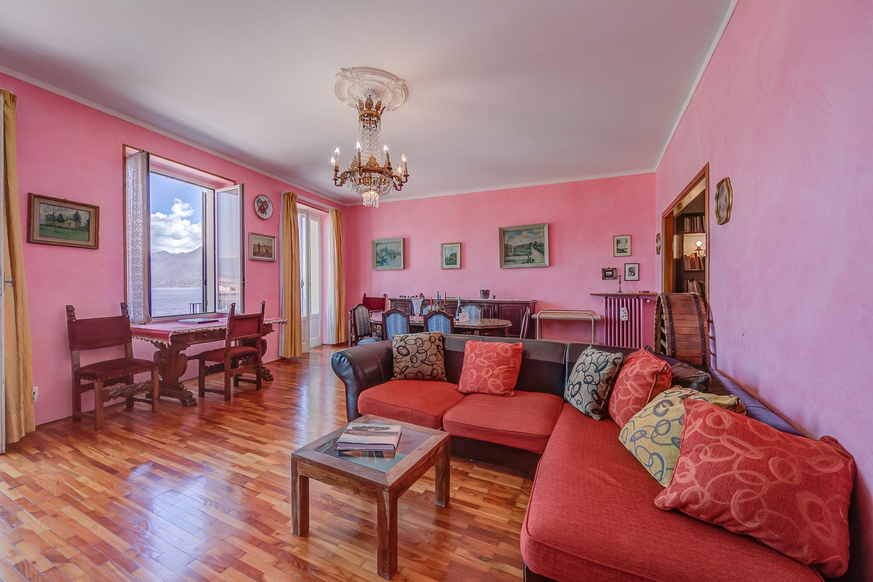 Ein Wohnzimmer mit Holzboden, einem roten Sofa, einem Esstisch mit Stühlen und einer Kristallleuchter.