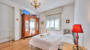 A bedroom with a wooden floor, a bed with white bedding, a red lamp on a bedside table, a wooden wardrobe, and a window with lace curtains. - Il Porticciolo Stresa (Stresa)