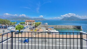 A coastal marina with boats docked, a road with vehicles, and a mountain in the background. - Il Porticciolo Stresa (Stresa)