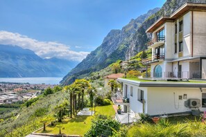 Ein modernes, zweistöckiges Gebäude mit Balkon, umgeben von üppiger Vegetation und Bergen.