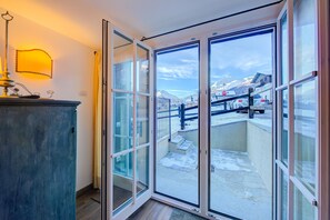 A room with a large sliding glass door leading to a balcony with a view of mountains and parked cars. - Chalet Charmant in Livigno (Livigno)