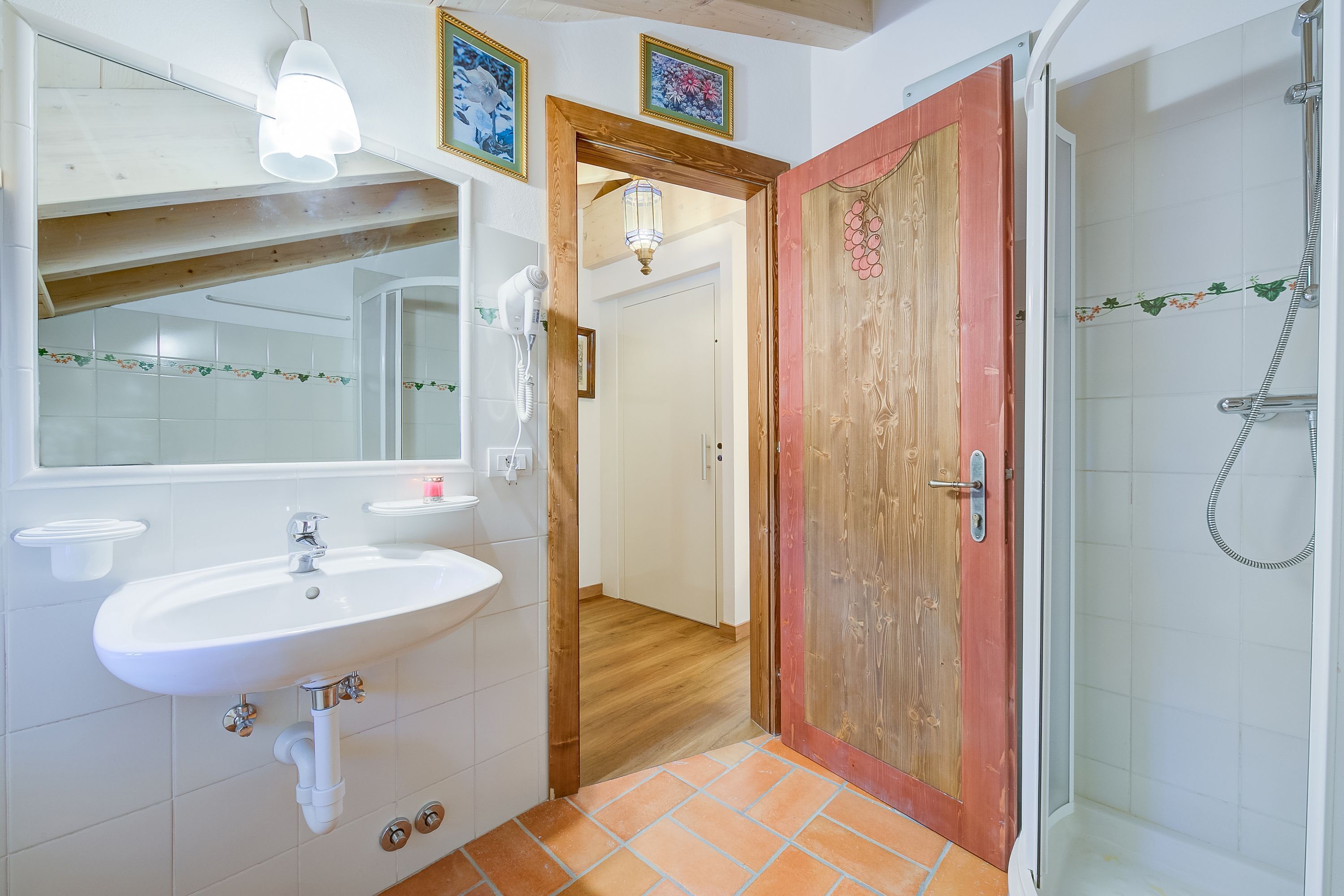 A bathroom with a white sink, a mirror, a shower, and a wooden door.