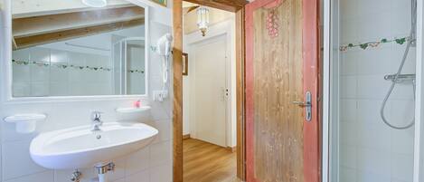 A bathroom with a white sink, a mirror, a shower, and a wooden door.