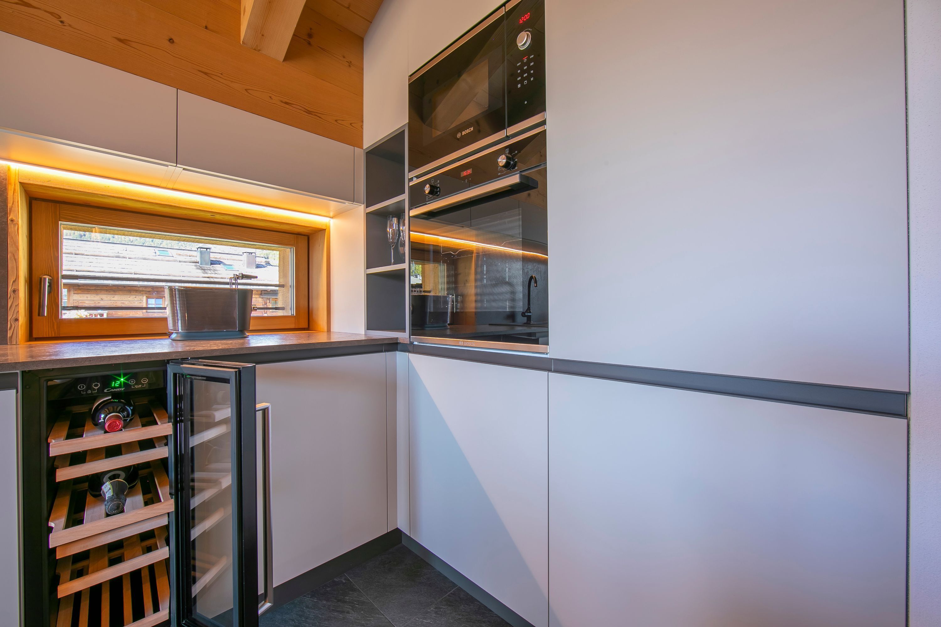Una cocina moderna con electrodomésticos integrados, un refrigerador de vinos y un ventanal que proporciona luz natural.