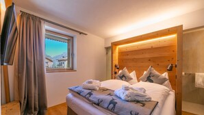 A bedroom with a wooden headboard, a window with a view of mountains, a bed with white linens, and a wooden bench. - Giulia in Livigno With 2 Bedrooms and 2 Bathrooms (Livigno)