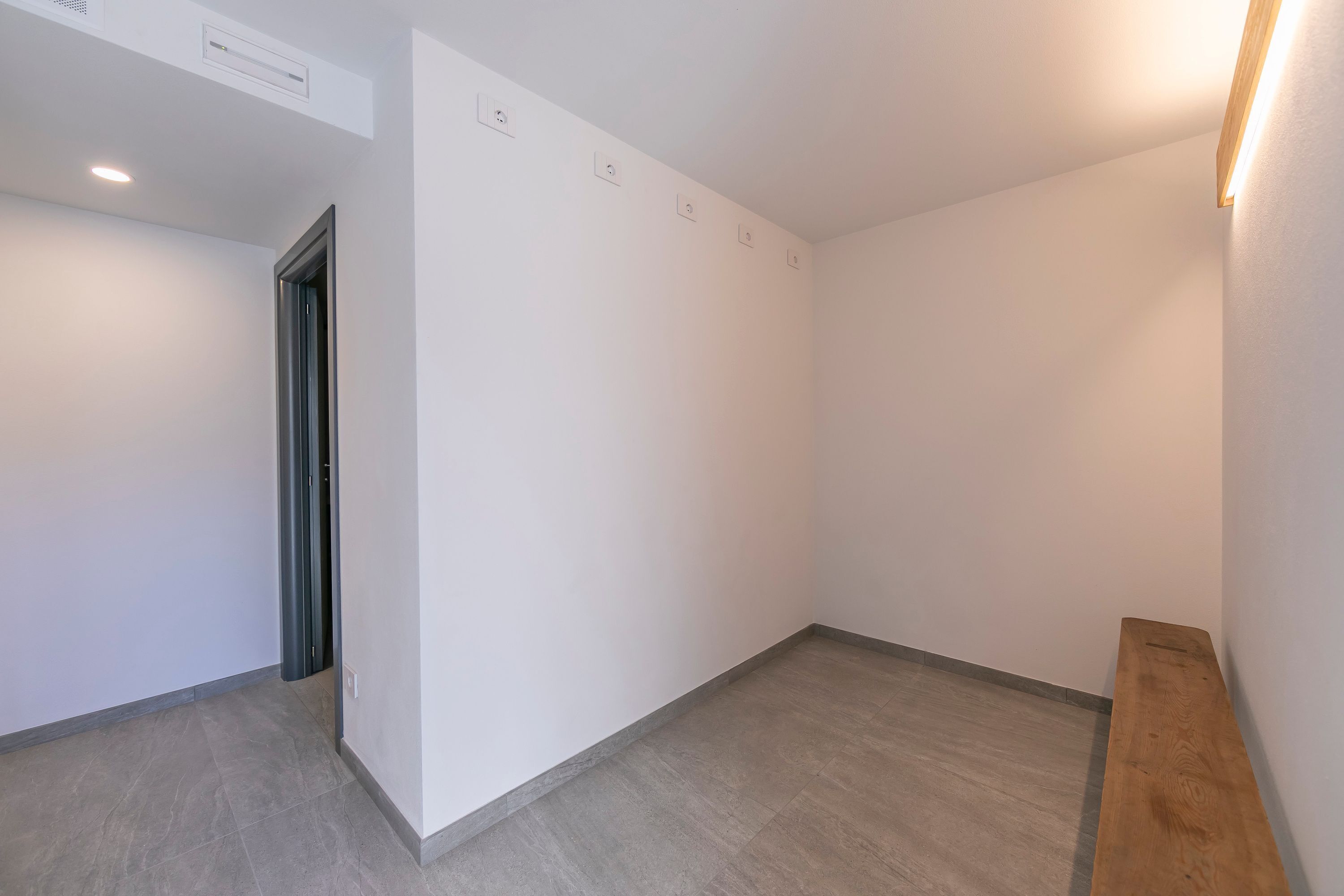 A clean, empty hallway with a wooden bench, white walls, and a tiled floor.
