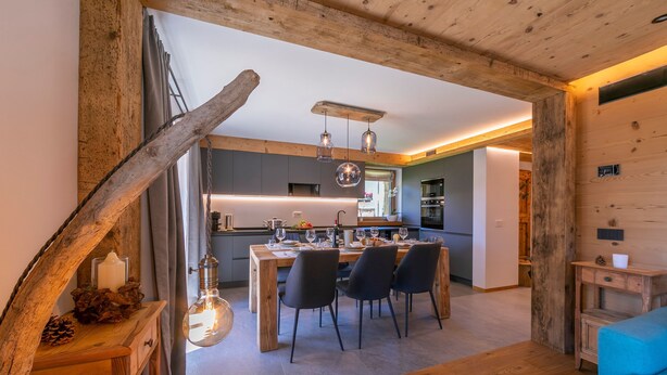 A modern kitchen with wooden beams, a dining area with a table and chairs, and a blue sofa in the foreground. - Giulia in Livigno With 2 Bedrooms and 2 Bathrooms (Livigno)