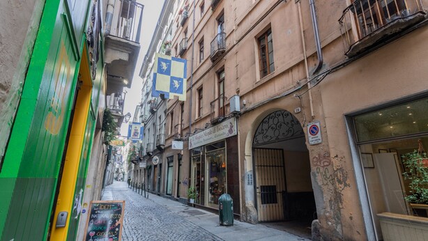 A narrow cobblestone street lined with buildings, a green door, and a signboard advertising a restaurant. - Barbaroux 10 - Luna by Wonderful Italy (Turin)