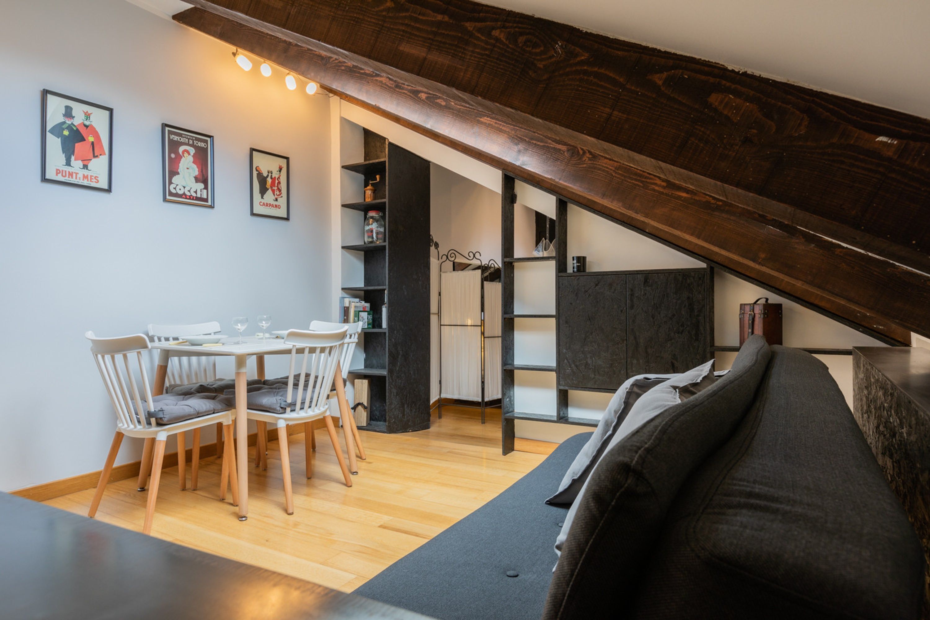 A dining area with a wooden table and chairs, a black sofa, and a staircase leading to an upper level.