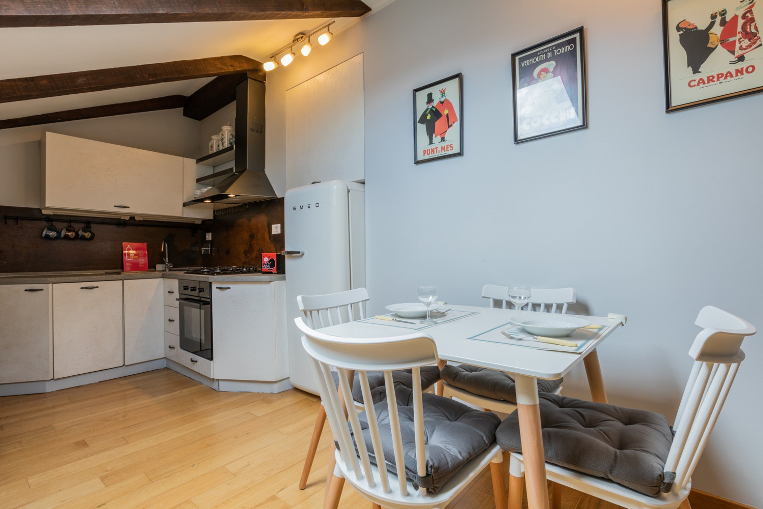 Une cuisine moderne avec des meubles blancs, une cuisinière et un réfrigérateur. On y trouve une table à manger avec des chaises et une affiche encadrée au mur.
