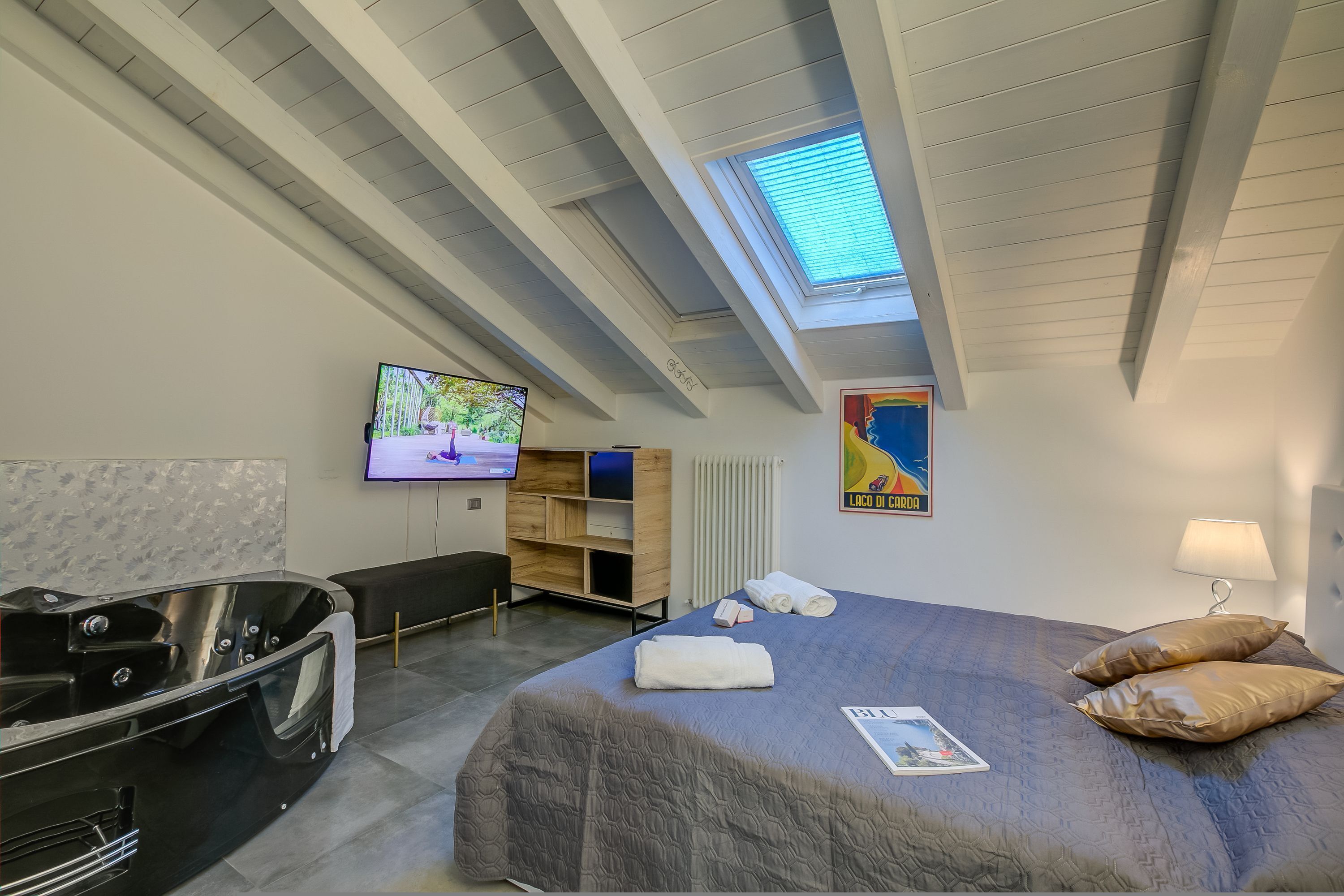 A modern hotel room with a skylight, a large bed, a TV, a desk, and a massage chair.