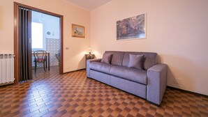 A living room with a patterned floor, a sofa, a dining table with chairs, a radiator, and a painting on the wall. - Nicoletta s Lake View On Stresa Hills (Stresa)