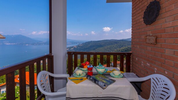 A balcony with a table set for breakfast, overlooking a scenic view of a lake and mountains. - Nicoletta s Lake View On Stresa Hills (Stresa)