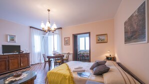 A hotel room with a bed, a TV, a dining table, chairs, and a chandelier. - Nicoletta s Lake View On Stresa Hills (Stresa)