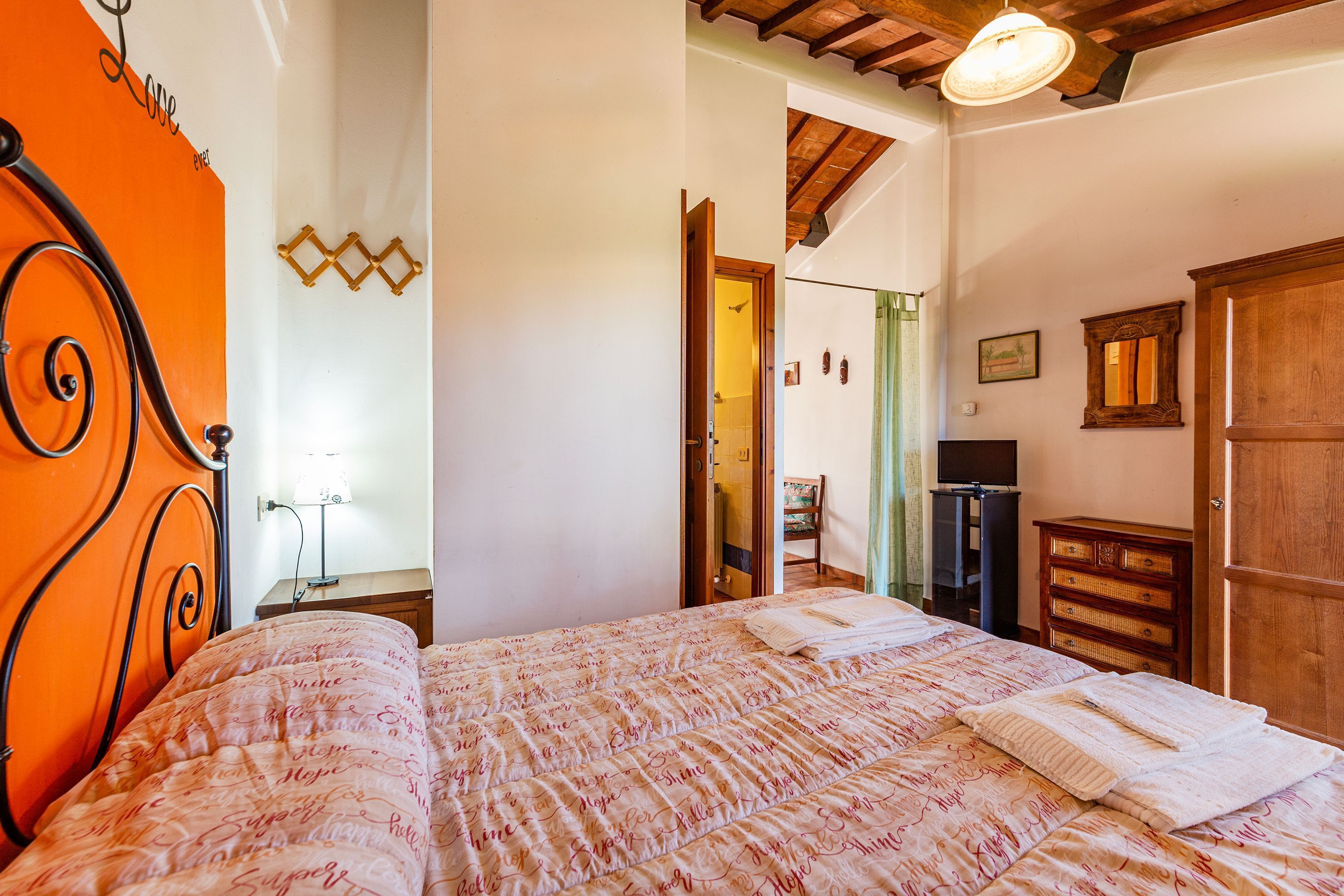 Un dormitorio con una cama, un aparador de madera, un escritorio con lámpara y un televisor.