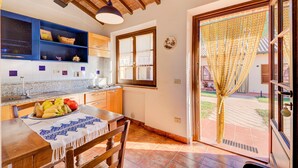 A kitchen with a wooden table, blue shelves, and a window with curtains. - Thyme apt With Shared Pool (Castiglione del Lago)