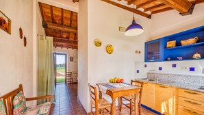 A kitchen with wooden cabinets, a blue shelf, and a dining table with chairs. - Thyme apt With Shared Pool (Castiglione del Lago)
