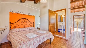 A bedroom with a bed, a wall with a motivational quote, a wooden ceiling, and a bathroom visible through an open door. - Thyme apt With Shared Pool (Castiglione del Lago)