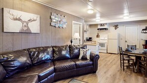 A modern living room with a leather sofa, a mounted deer head artwork, and a wall-mounted photo collage. - Moose Hollow Apartment (Greenville)