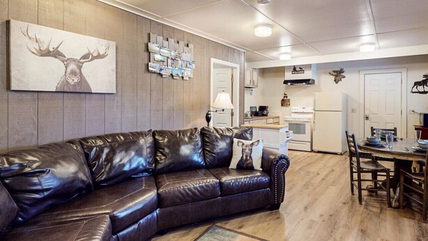 A modern living room with a leather sofa, a mounted deer head artwork, and a wall-mounted photo collage. - Moose Hollow Apartment (Greenville)