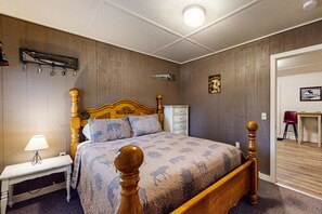 Un dormitorio con cama de madera, una mesita de noche con lámpara, un aparador y un escritorio con silla.