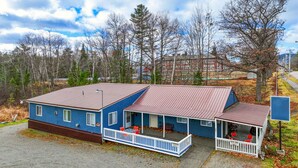 A two-story building with a blue exterior and a red roof, featuring a porch with red chairs and a small table. - Moose Hollow Apartment (Greenville)